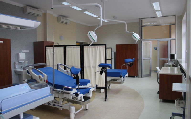 Zdjęcie bloku porodowego. Łóżka szpitalne, oddzielone parawanami. Nad nimi lampy szpitalne.