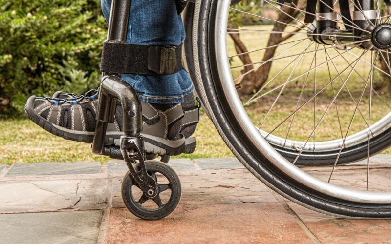 Fragment wózka inwalidzkiego. Na platformie wózka zdjęcie stóp człowieka siedzącego na wózku.