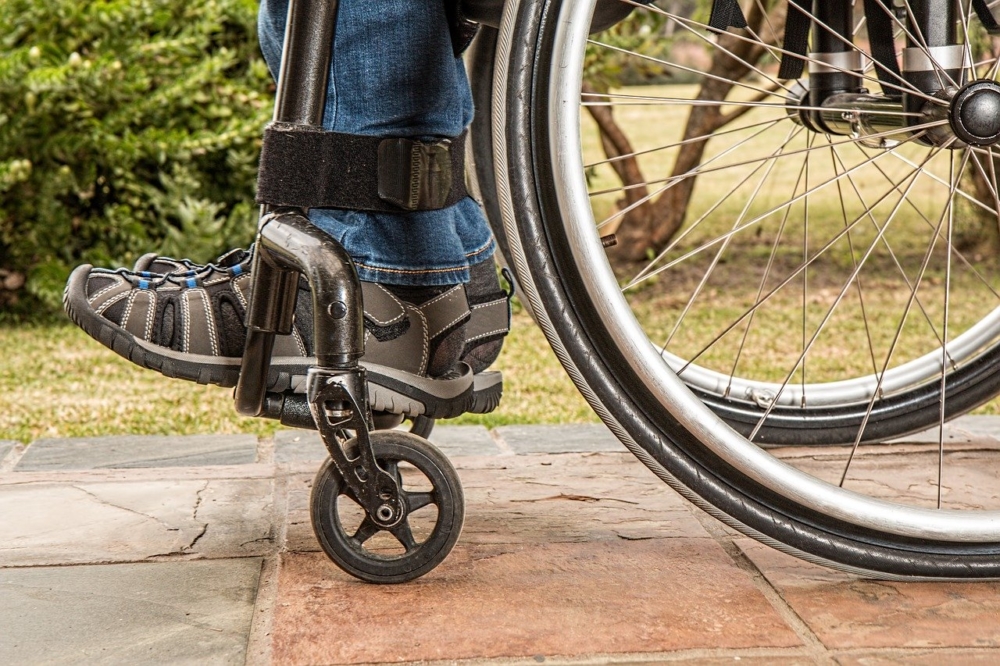 Fragment wózka inwalidzkiego. Na platformie wózka zdjęcie stóp człowieka siedzącego na wózku.