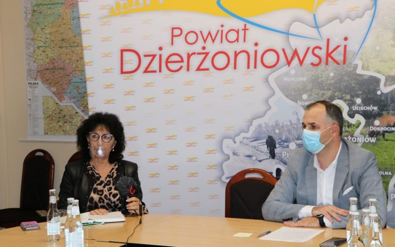 Na zdjęciu dwie osoby siedzące za stołem w maseczkach ochronnych. W tle ścianka promocyjna z napisem powiat dzierżoniowski.