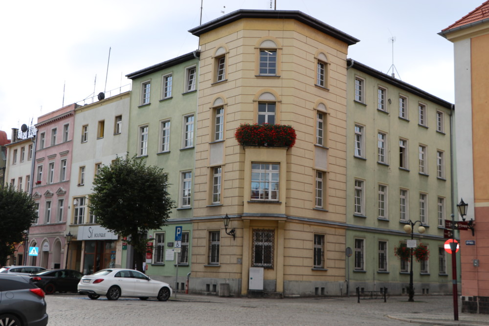 Na zdjęciu budynek starostwa powiatowego w rynku w Dzierżoniowie. Widać budynek w kolorze żółto-zielonym. Przed budynkiem zaparkowane samochody.