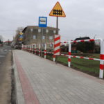 Na zdjęciu nowy chodnik z kostki betonowej wraz z barierkami ochronnymi i znakami drogowymi. W tle widać budynek wielorodzinny