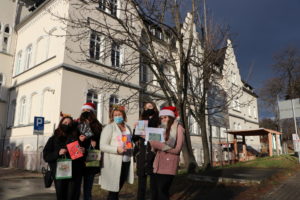 Na pierwszym planie 4 uczennice i nauczycielka trzymają kartki świąteczne. W dalszym planie budynek szpitala powiatowego w dzierżoniowie