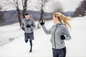 Na zdjęciu widać biegnąca parę - kobietę oraz mężczyznę, w zimowej scenerii. Kobieta wyciągniętym palcem zaprasza mężczyznę do dalszego biegu.