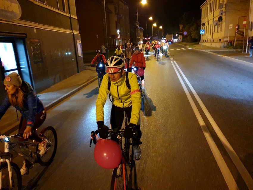 Uczestnicy jadą ulicą - prawym psem - z Bielawy do Dzierżoniowa. Jest już ciemno ulice oświetlają latarnie i lampki rowerów.