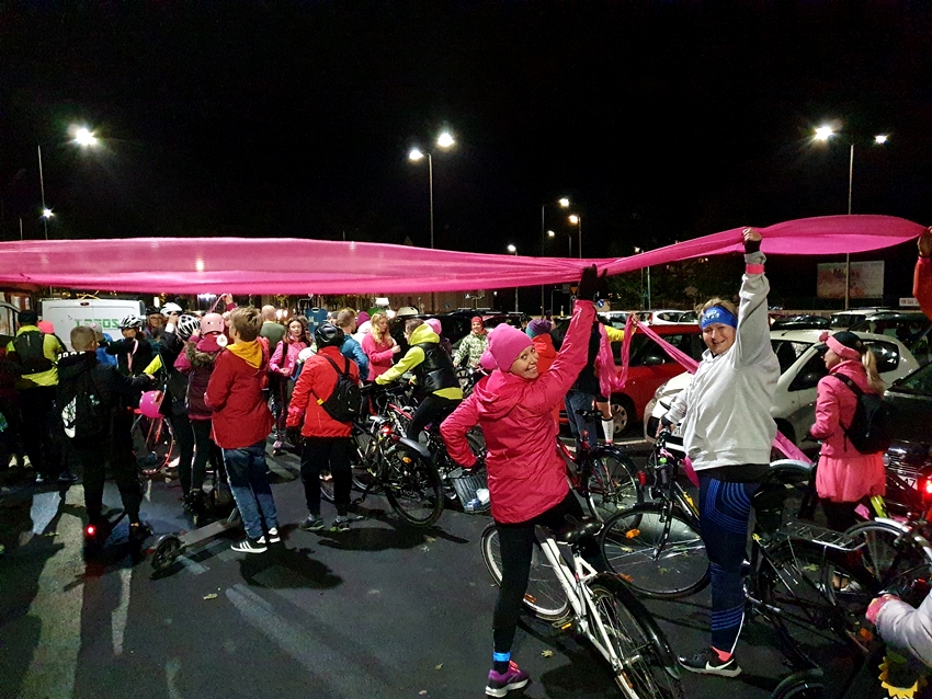 Zdjęcie wydarzenia. Na zdjęciu uczestnicy trzymają różową wstęgę i swoje rowery do przejazdu wyznaczonej trasy.