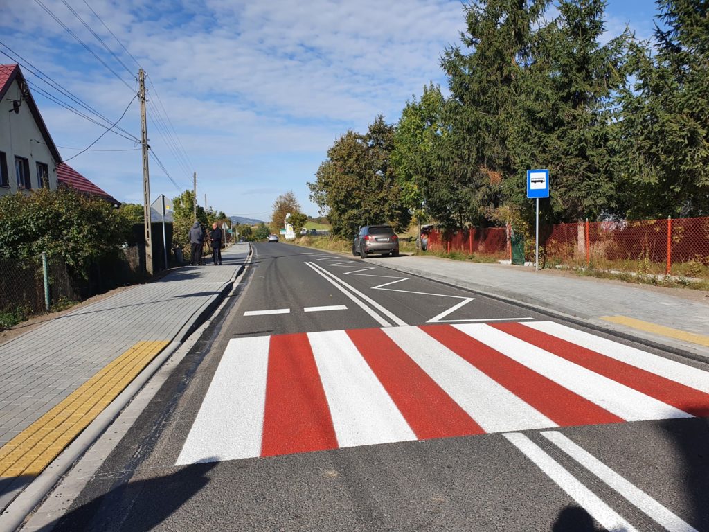 Droga z Bielawy - Józefówka. Na zdjęciu biało-czerwone przejście dla pieszych. Po obu stronach drogi chodnik i zabudowa.