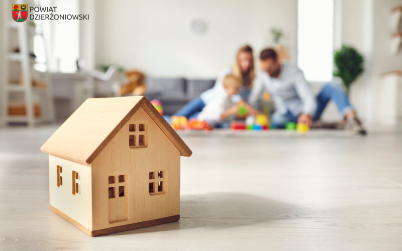 grafika przedstawiająca drewniany zabawkowy dom i rodzinę w tle