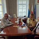 trzy osoby siedzą przy stole, a na stole leżą medale