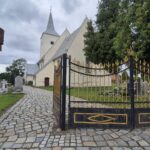 kościół z zewnątrz, widok zza bramy, wokół cmentarz, na jego terenie drzewo.
