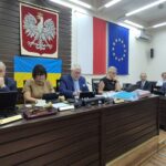 przewodniczący rady i wiceprzewodniczący siedzą przy stole, w tle zarząd powiatu