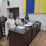 sekretarz, radca prawny i skarbnik siedzą przy stole, w tle dwie kobiety na krzesłach
