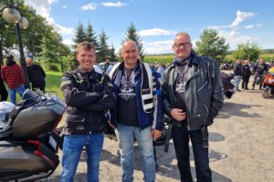 Trzech mężczyzn, w tym starosta, w tle motocykle