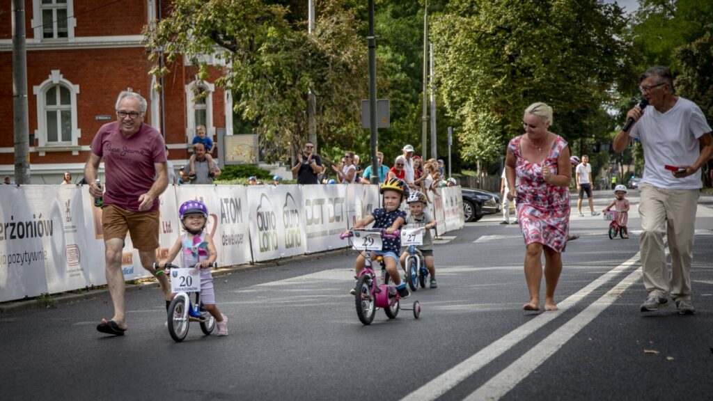 Troje dorosłych i dwoje dzieci na rowerkach jadą po ulicy.