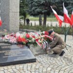 mężczyzna w mundurze kuca pod pomnikiem, żeby złożyć kwiaty