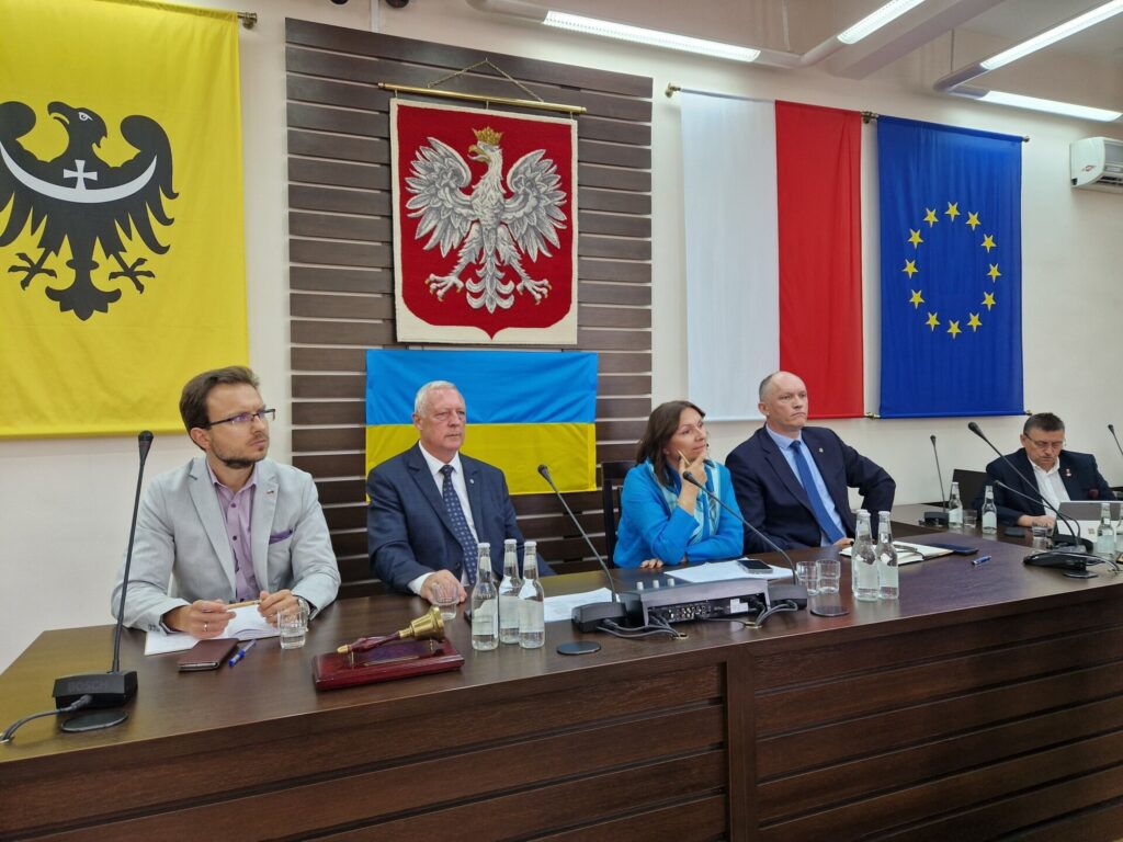 widok na gospodarza spotkania, który siedzi z innymi przy stole prezydium rady
