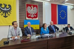 widok na gospodarza spotkania, który siedzi z innymi przy stole prezydium rady
