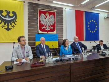 widok na gospodarza spotkania, który siedzi z innymi przy stole prezydium rady