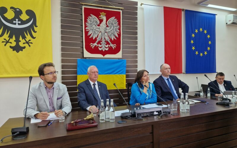 widok na gospodarza spotkania, który siedzi z innymi przy stole prezydium rady