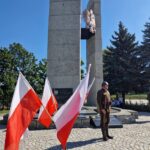pomnik pamięci losów ojczyzny, pod nim tablice, flagi i osoba w mundurze