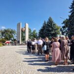 ludzie stoją i czekają na złożenie kwiatów pod pomnikiem, widok od tyłu naprzeciwko pomnika
