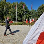 mężczyzna składa kwiaty pod pomnikiem