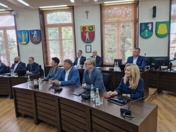 zaproszeni goście siedzą przy stołach na sali sesyjnej