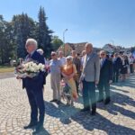 ludzie stoją i czekają na złożenie kwiatów pod pomnikiem