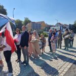 ludzie stoją i czekają na złożenie kwiatów pod pomnikiem