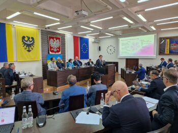zaproszeni goście siedzą przy stołach na sali sesyjnej, widok na stół prezydium rady, gdzie siedzi gospodarz spotkania z innymi ludźmi
