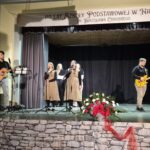 koncert, dzieci na scenie śpiewają, 2 osoby grają na gitarze