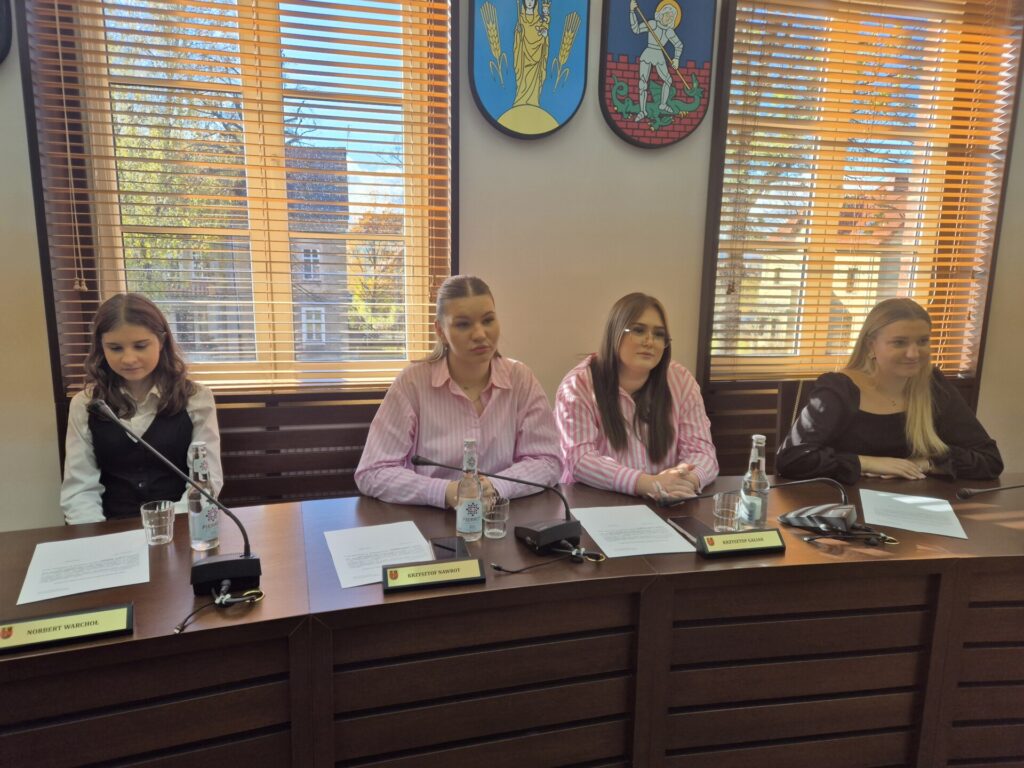 dziewczyny siedzą przy stole, na ścianach herby