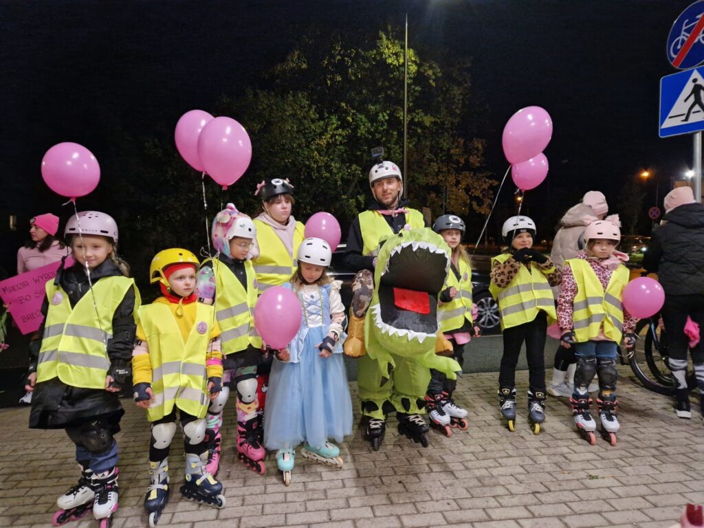 dzieci na rolkach w odblaskowych kamizelkach, opiekun ma przebranie dinozaura