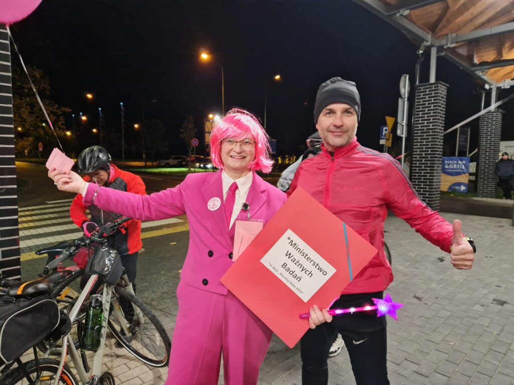 wicestarosta i radna miasta Dzierżoniów ubrana w różowy garnitur i różową perukę trzyma różową księgę z napisem Ministerstwo Badań Ważnych