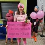 kobieta w różowym stroju stoi z różową dużą kartką z napisem: Madzia Wyrolowała, bo się badała. Bądź jak Madzia.