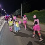 widok z tyłu, dwie uczestniczki w różowych spódniczkach biegną, obok dzieci na rolkach