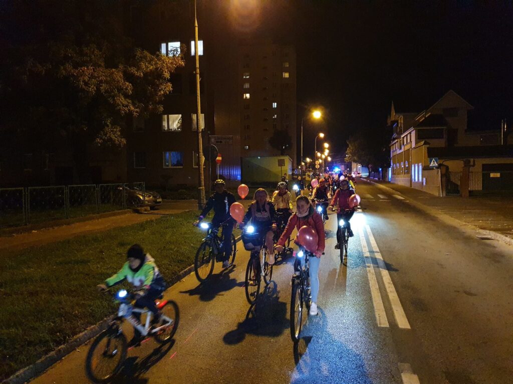 ludzie jadą wieczorem ulicą na rowerach