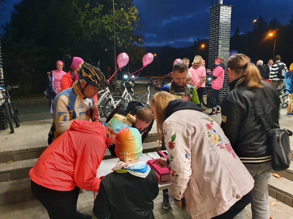 ludzie nad stolikiem się pochylają, w tle osoby z różowymi balonami