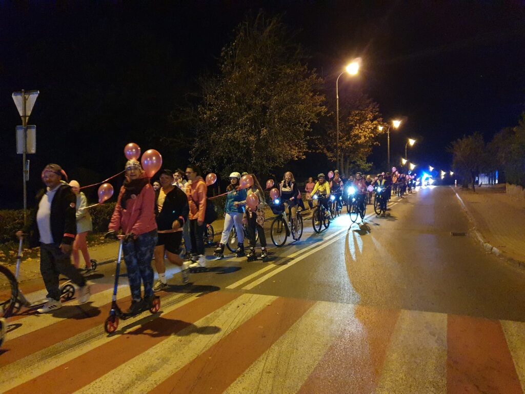 ludzie jadą z różowymi balonami na hulajnogach, rowerach