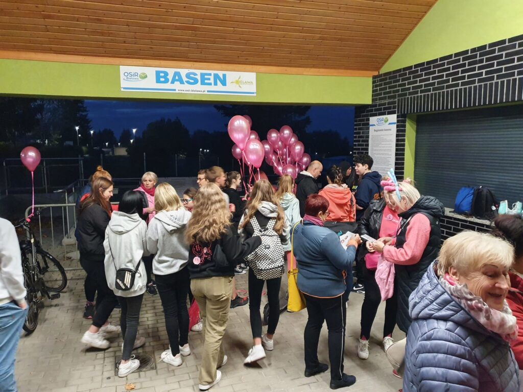 ludzie z różowymi balonami, od góry napis basen