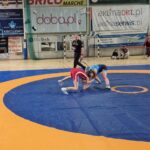 zapaśniczki podczas rywalizacji na macie, w tle sędzia