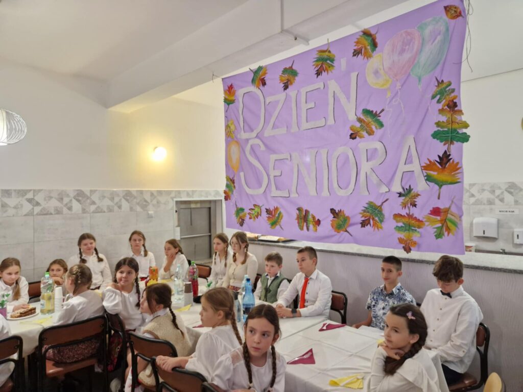 dzieci siedzą przy stoliku, w tle napis dzień seniora na różowym tle