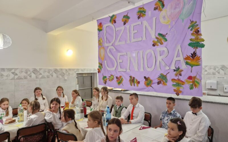 dzieci siedzą przy stoliku, w tle napis dzień seniora na różowym tle