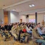 uczestnicy ćwiczeń siedzą w budynku na krzesłach