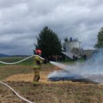 strażacy gaszą płonące trawy wężami strażackimi, wokół dym