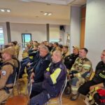 przedstawiciele straży i policji siedzą na krzesłach, widok z profilu