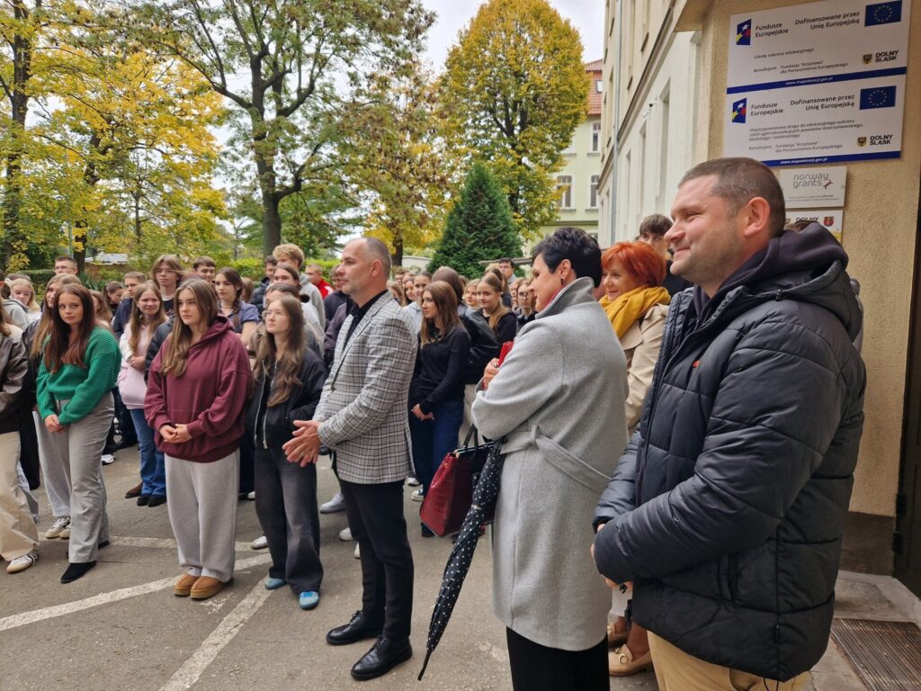 grupa uczniów, wicestarosta i dyrektor wydziału edukacji stoją pod szkołą