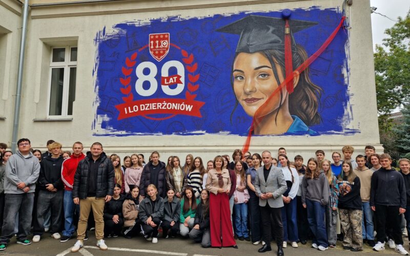 grupa uczniów wraz z dyrektor i wicestarostą stoją pod muralem z okazji 80-lecia I LO