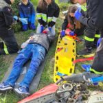 MDP w strojach straży podczas ćwiczeń, jedna osoba leży na ziemi, obok nosze i rozbity motor