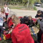 MDP w czerwonych strojach podczas ćwiczeń, jedna osoba leży unieruchomiona na noszach